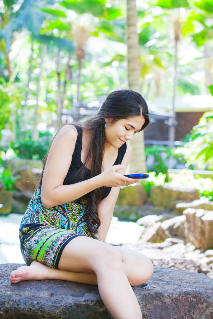 Biracial teen girl sitting on rock looking at cellphone Teen girl looking at her cellphone